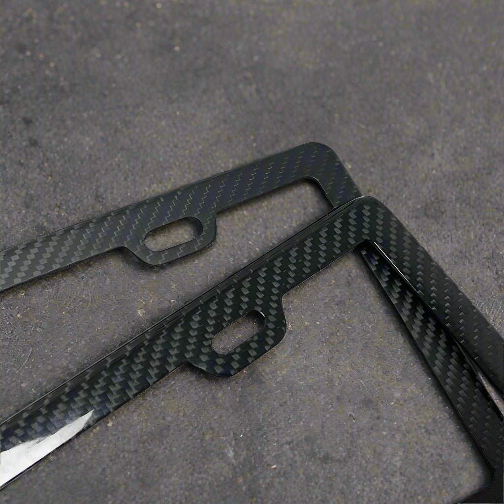 Two black carbon fiber license plate frames on a white background