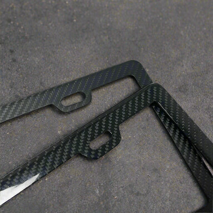 Two black carbon fiber license plate frames on a white background